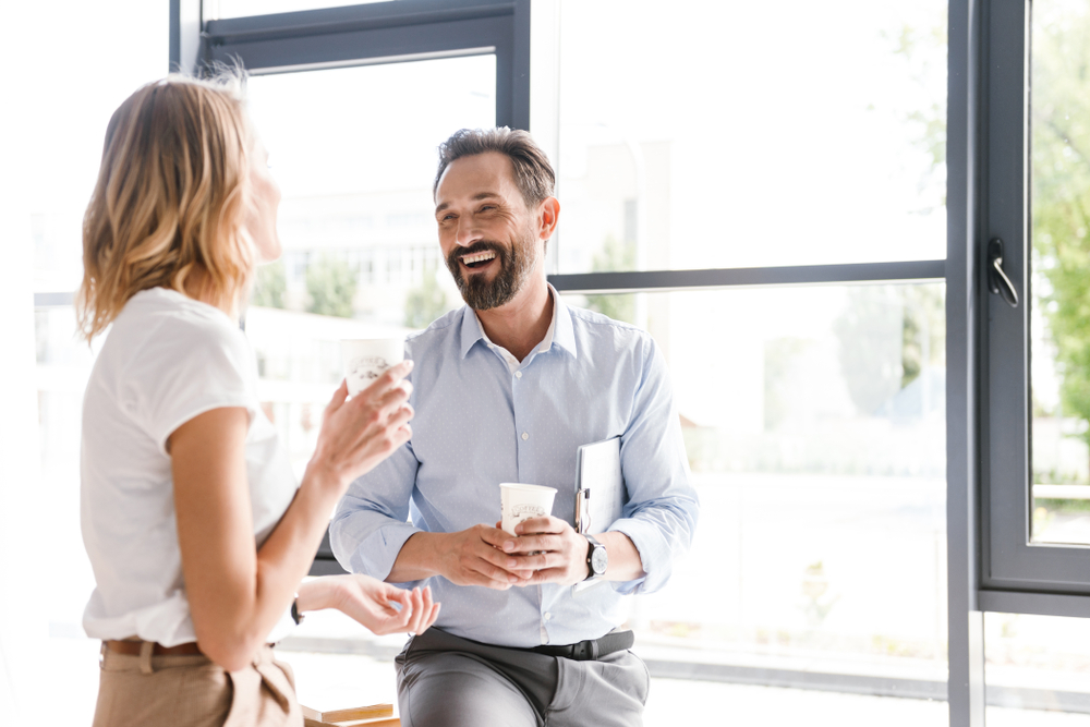 女性と男性が窓際でコーヒーを飲みながら談笑している